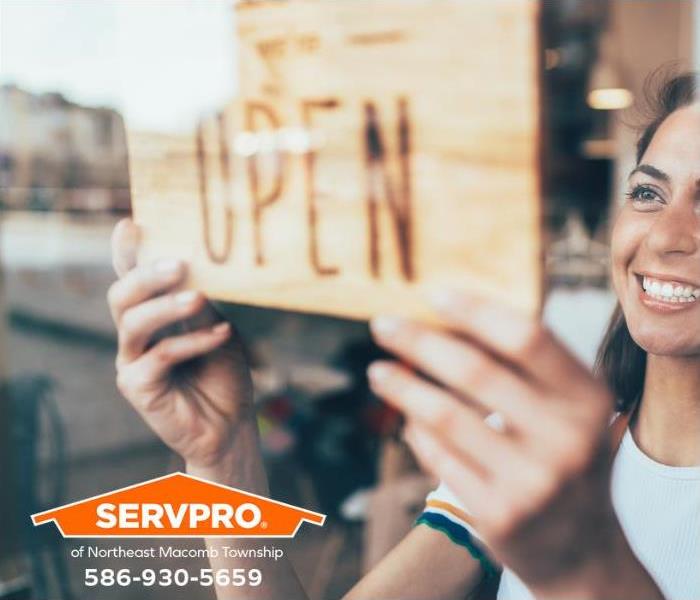 A happy business owner places an “open” sign on the front door.