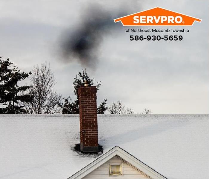 Smoke rises from a chimney with signs of soot buildup at its base. 